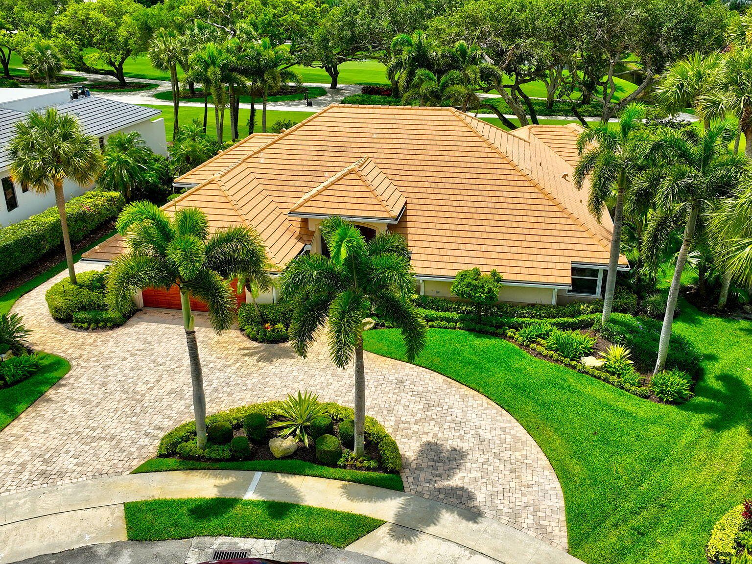 Aerial of 4960 Cherry Laurel Lane from the front, the tile hip roof centered between mature palms with the circular paver driveway sweeping in from the cul-de-sac