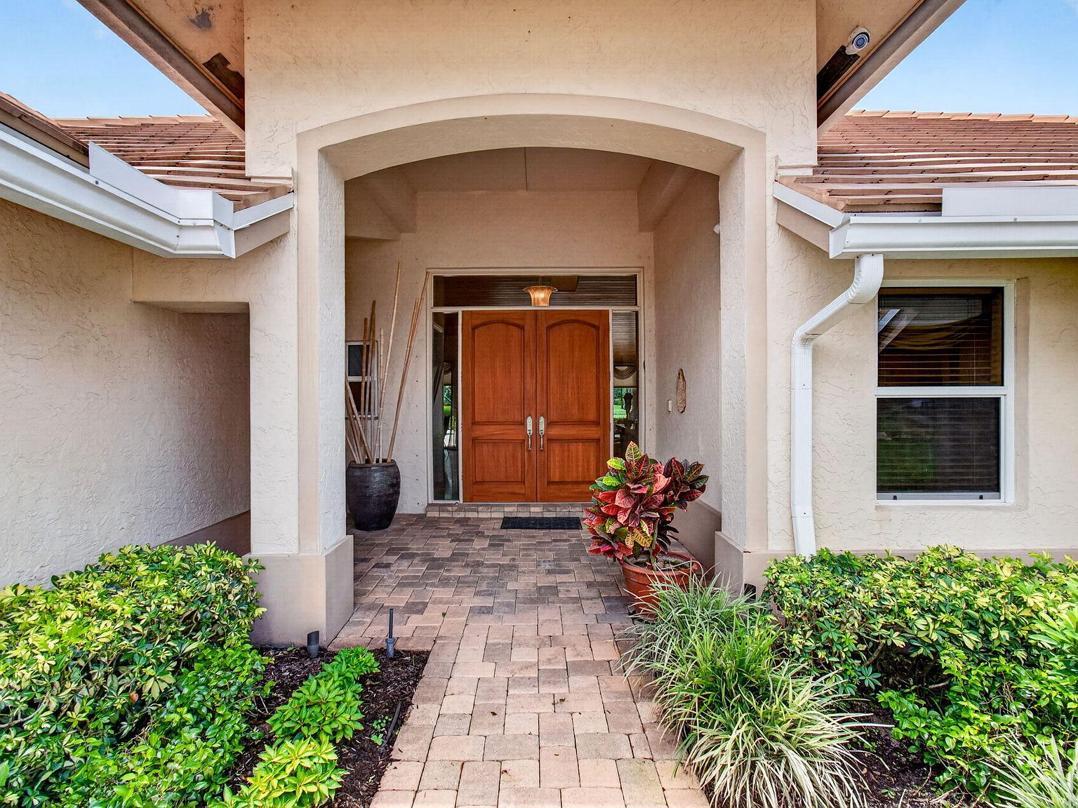 Close detail of the arched entry porch: mahogany double doors, terracotta tile floor, and tropical plantings flanking the path
