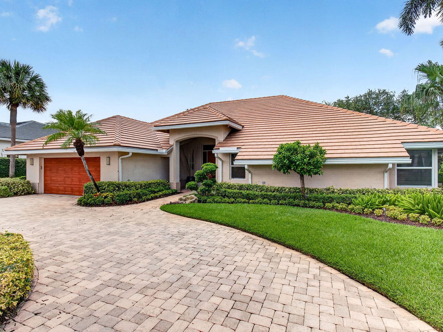 The home read in full afternoon light: tile hip roof, arched entry, hedge line, and lawn carrying the eye toward the door